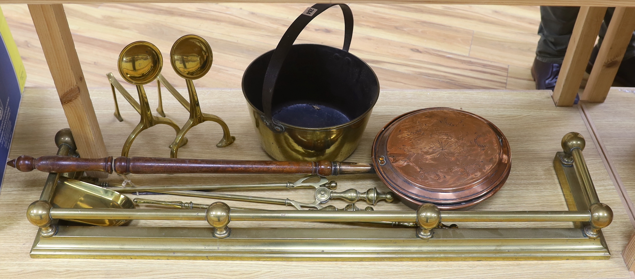 Brassware including fire kerb, fire tools, arts and crafts fire dogs and a copper warming pan, the largest 116cm wide